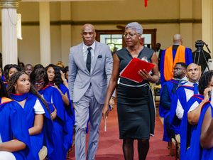 Academic officials in blue graduation robes walking down the aisle at a university ceremony.