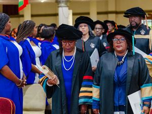 Academic procession with faculty in doctoral regalia carrying diplomas at graduation.