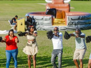 People cheering with black pom-poms at an outdoor event with an inflatable mechanical bull ride in the background.