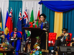 Woman in academic regalia delivers speech at podium during graduation ceremony.