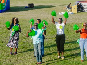 People cheering with green pom-poms on a grass field during an outdoor community sports event.