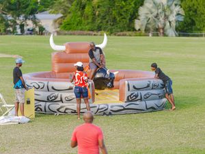 Group of people enjoying an inflatable mechanical bull ride attraction at an outdoor festival event.