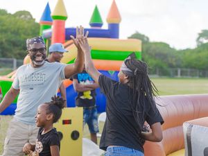 Man and woman high-five near a colorful inflatable bounce castle at an outdoor family fun event with a child nearby.