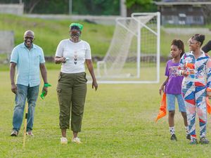 Adults and children walking on a sports field with a soccer goal in the background during an outdoor event.
