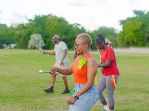 Woman in orange top playing golf outdoors on green field with friends during casual daytime activity.