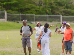 Group of people socializing and playing outdoor sports on a green field in a tropical setting.