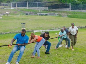 A group of people enthusiastically playing tug of war on a green grassy field at an outdoor event.