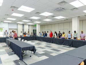 Group of people standing around conference tables in a modern meeting room during a formal gathering or workshop.