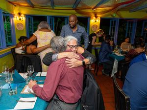 Guests hugging and mingling at a colorful restaurant dinner event with blue tables and yellow walls.