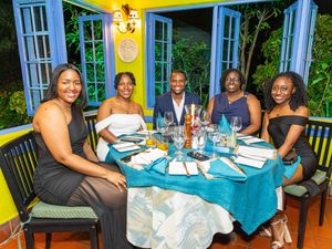 Five friends smiling at a elegantly set dining table with teal tablecloth at a tropical restaurant.