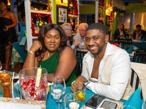 Two people smiling at a festively decorated restaurant table with candles and holiday decor.