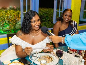 Woman in white dress being interviewed at a tropical restaurant dinner with red wine on the table.