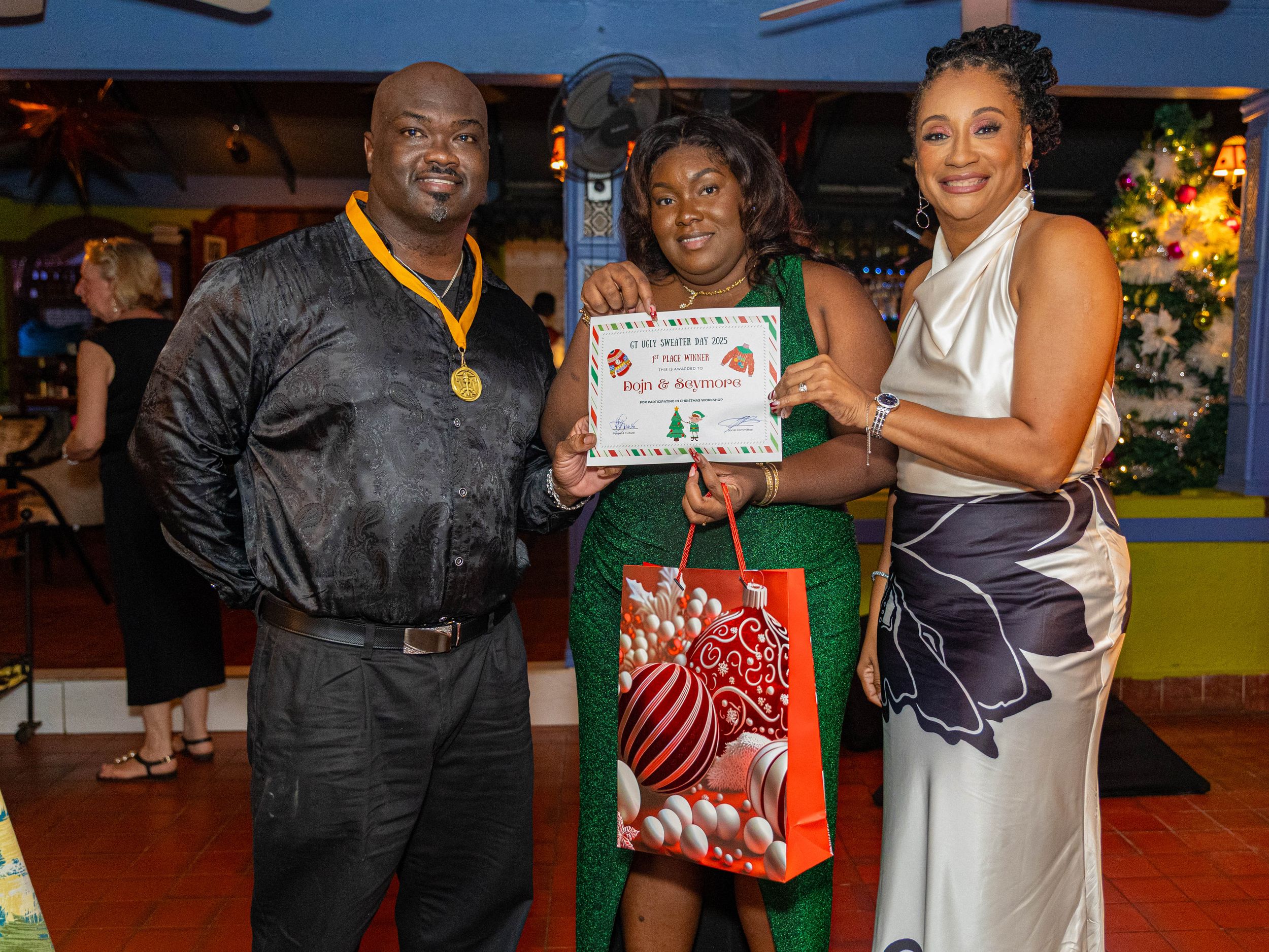 Three people posing with a certificate and gift bag at a festive holiday awards ceremony indoors.