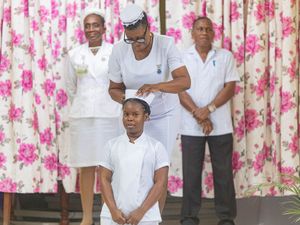 A nurse places a cap on a young girl in white uniform during a nursing pinning ceremony indoors.