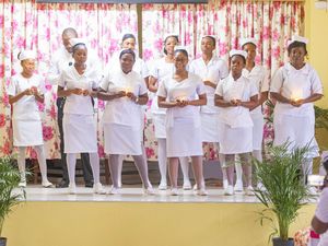 Group of nurses in white uniforms holding candles on stage during a nursing graduation ceremony.