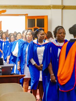 Women in blue graduation gowns processing during a university commencement ceremony indoors.