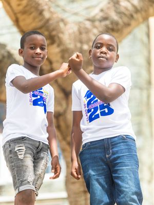 Two young boys in matching white Class of 25 shirts doing a handshake outdoors.