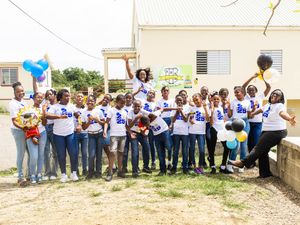 Large group of young people in matching white t-shirts celebrating outdoors with balloons near a building.