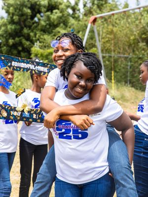 Two smiling students in Class of 2025 graduation shirts embrace outdoors at celebration event.