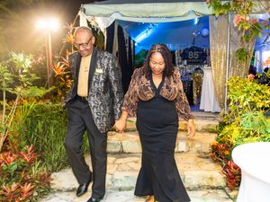 Couple holding hands walking through a beautifully lit outdoor garden party at night.