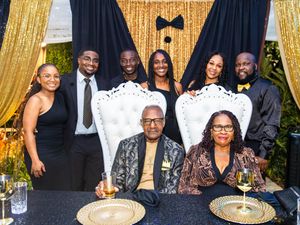 Family group photo at elegant gold and black themed celebration with eight people posing at decorated table.