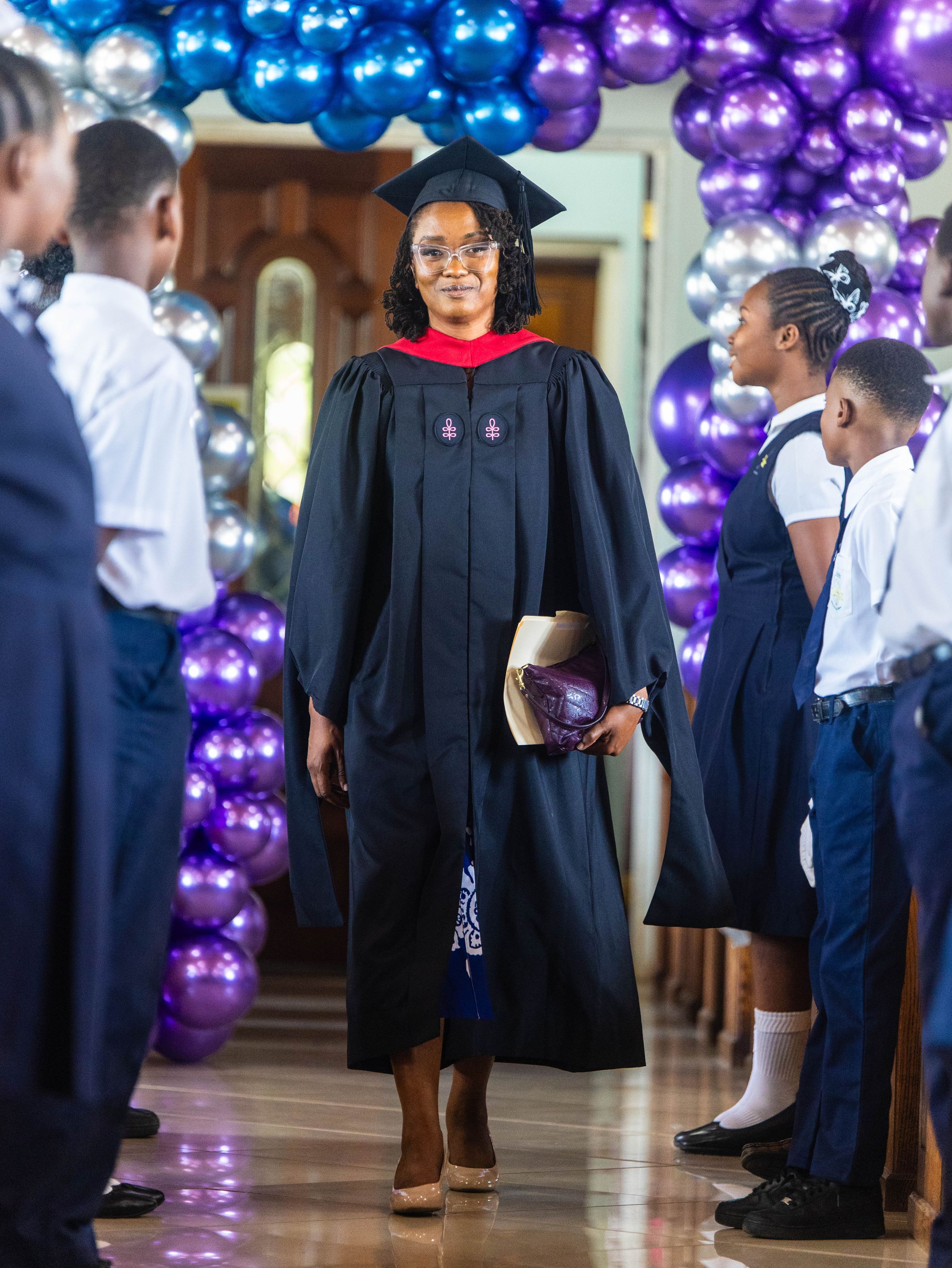 Graduate in black cap and gown walks through balloon arch at SDA Academy graduation ceremony 2025.