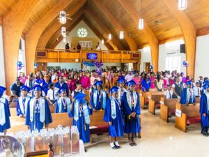 Graduation ceremony in a church with students in blue caps and gowns standing among pews filled with attendees.