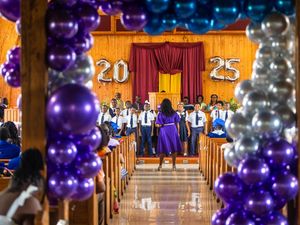 Graduation ceremony in church decorated with purple and silver 2025 balloons and graduates in blue.