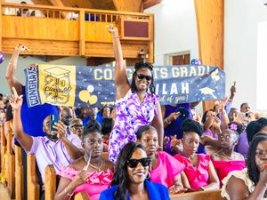 Proud family members cheer and hold congratulations signs at graduation ceremony in packed church.