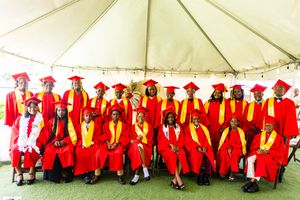 Large group of graduates in red caps and gowns with gold CCPS stoles pose together under tent.