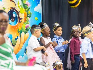 Diverse kindergarten children perform on stage wearing crowns at a school event.