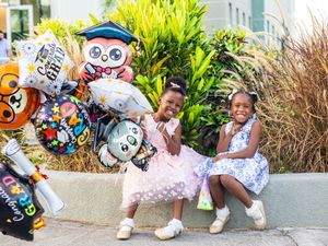 Two young girls in dresses pose with graduation balloons outdoors, celebrating a special milestone together.