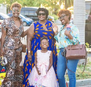 Three women and a young girl in festive attire smile together outdoors at a celebration.