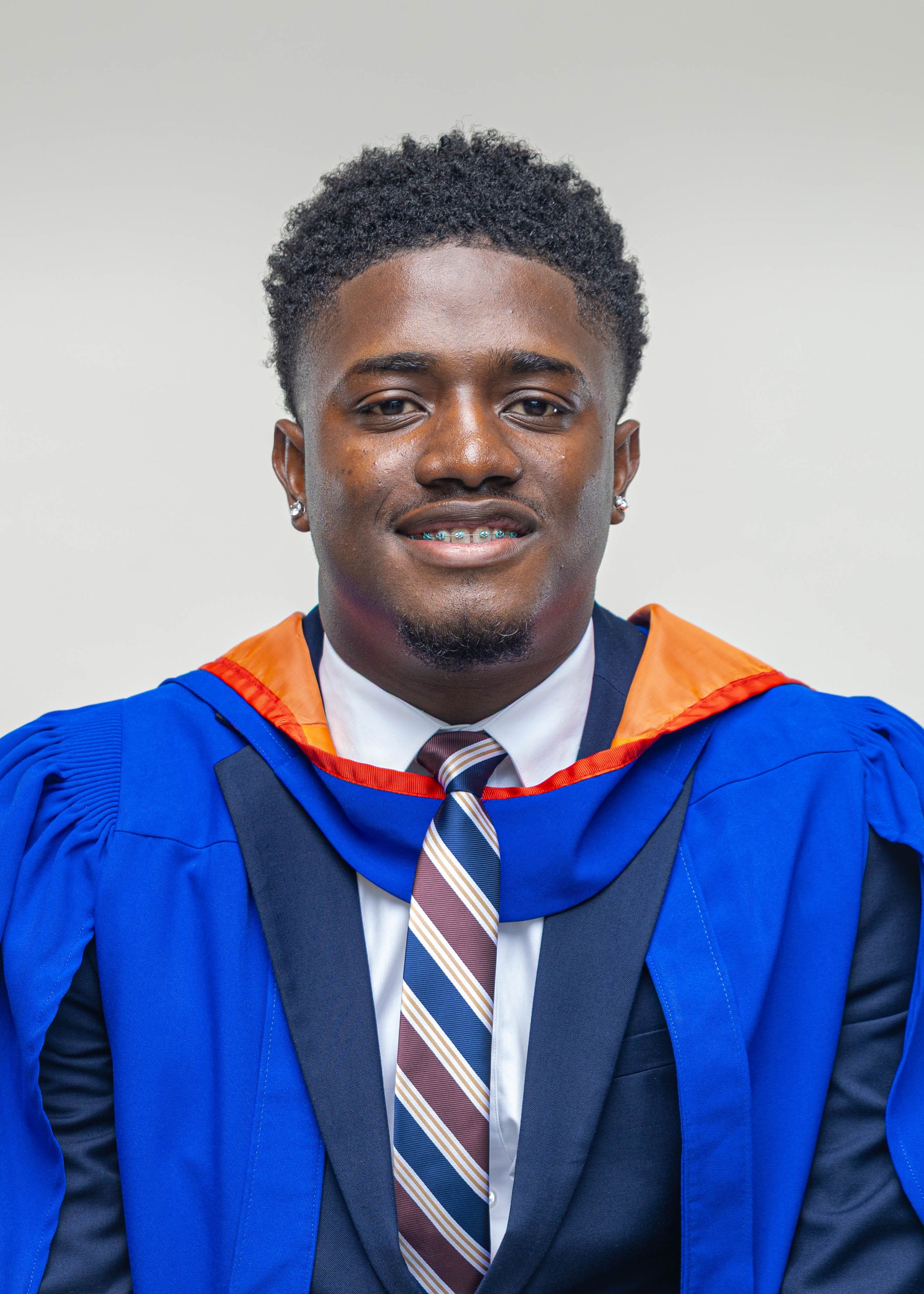 Young man in blue graduation gown with orange hood wearing striped tie at commencement.