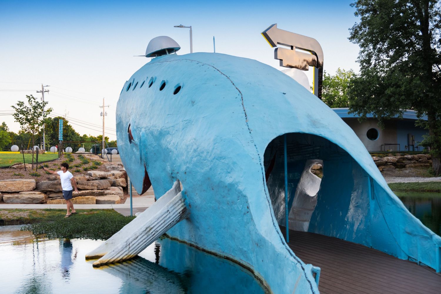 5. A young man casts his fishing line into the pond while standing next to the Blue Whale of Catoosa. Route 66 can be seen in the background