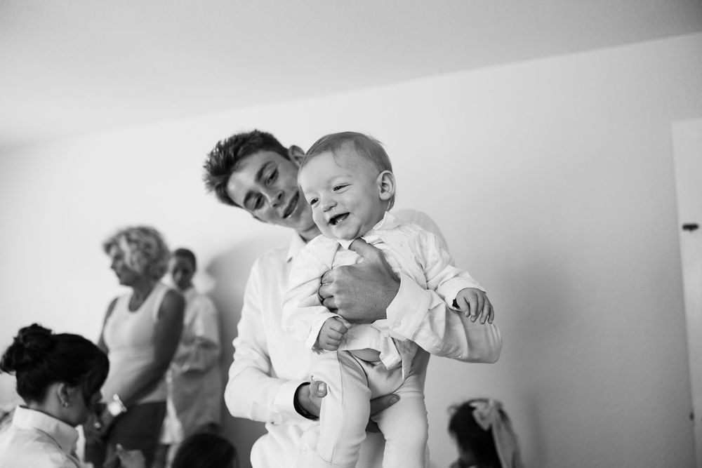 Black and white photo of a young man holding a laughing baby at a wedding celebration.