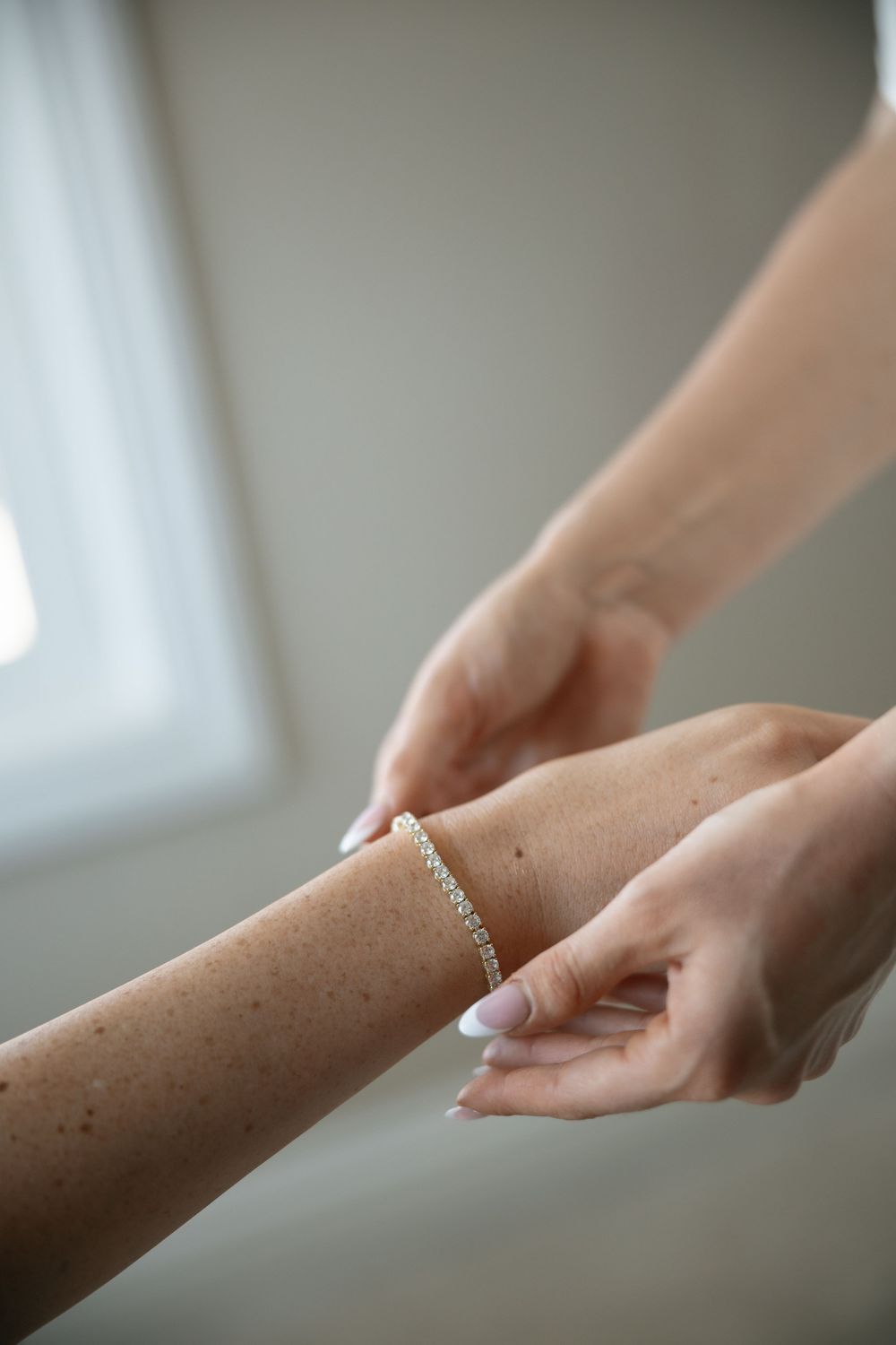 Close-up of hands clasping a delicate diamond tennis bracelet on a woman's wrist.