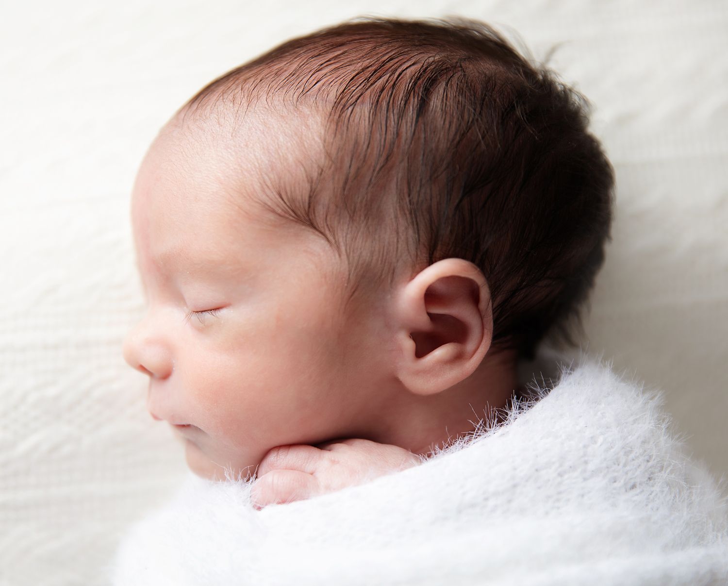Peaceful newborn baby sleeping wrapped in a soft white blanket with dark hair, perfect newborn photography portrait in Bexley