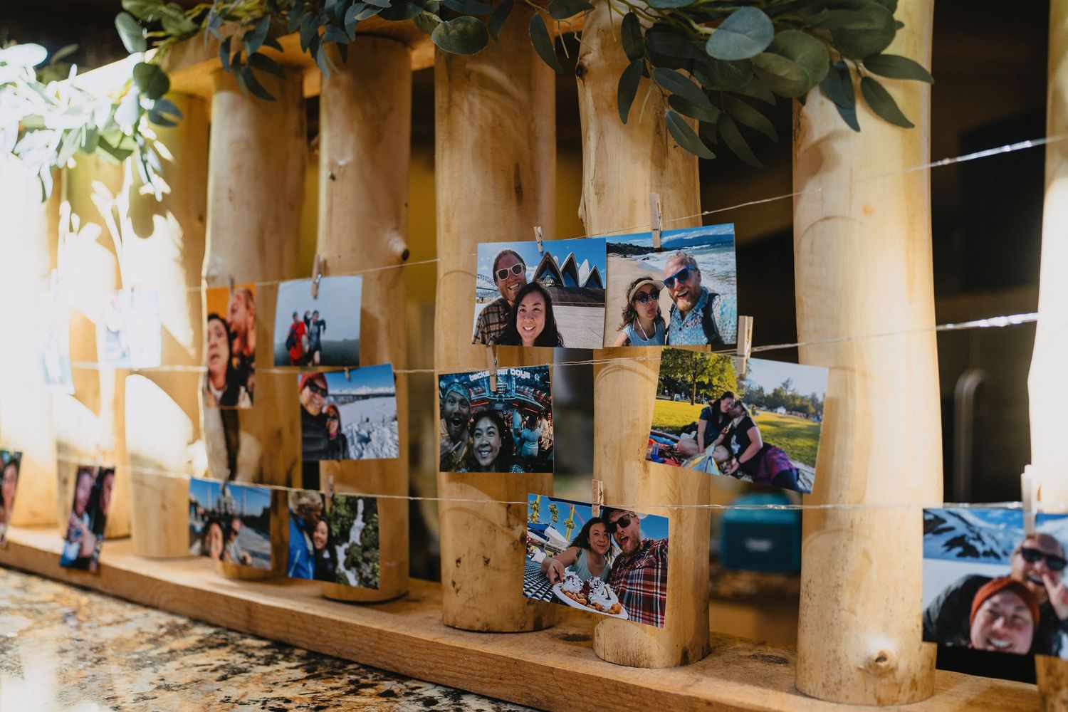 Wedding photo display with couples pictures clipped to string lights on rustic wooden columns.