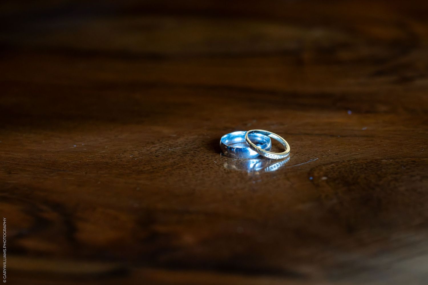 Two gold wedding rings resting on a dark wooden surface with soft bokeh lighting.