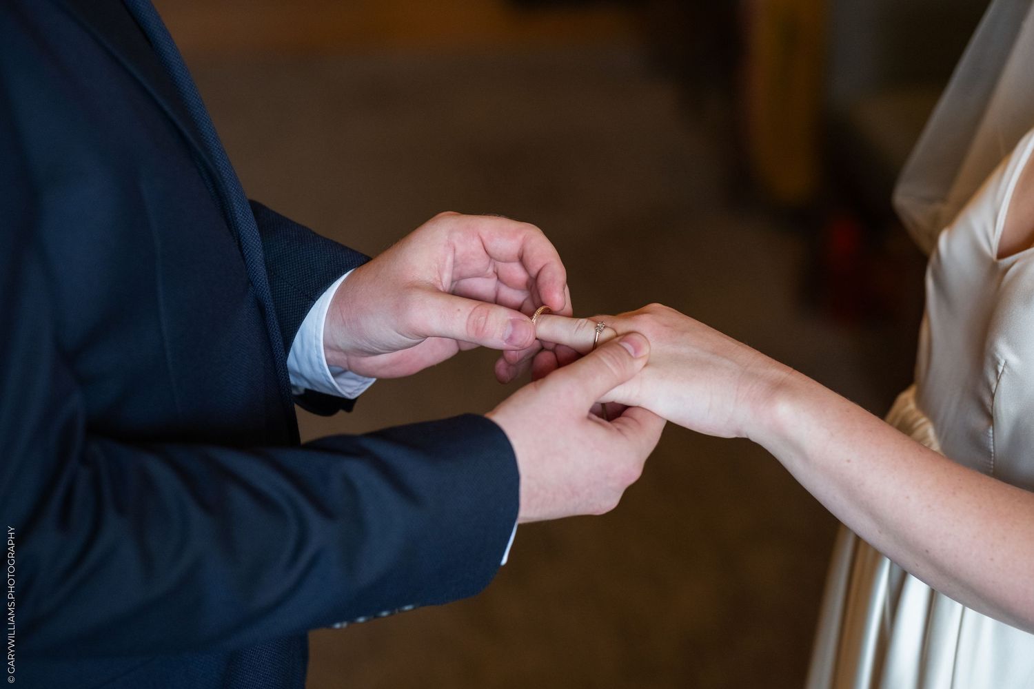 Groom placing a wedding ring on brides finger during a wedding ceremony.