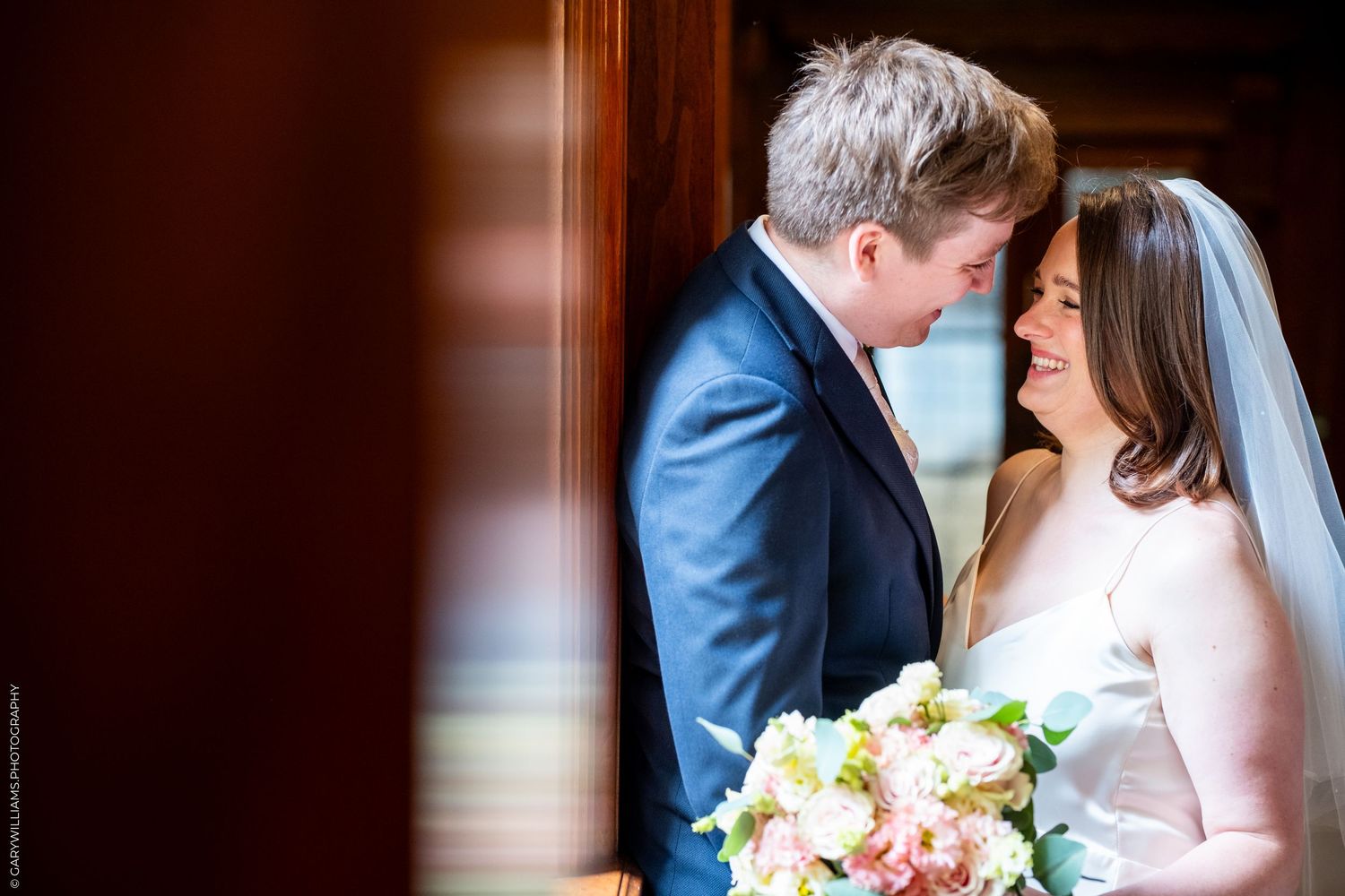 Bride and groom share an intimate moment, bride holding a pink and white bouquet, groom in navy suit.