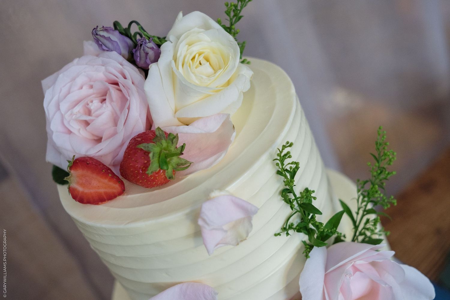 Elegant two-tier white wedding cake decorated with fresh roses, strawberries, and greenery.