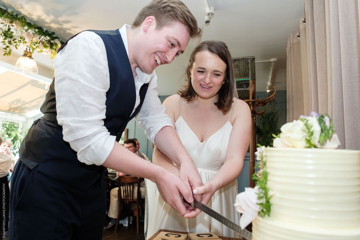 Bride and groom smiling while cutting their white wedding cake together at their reception.