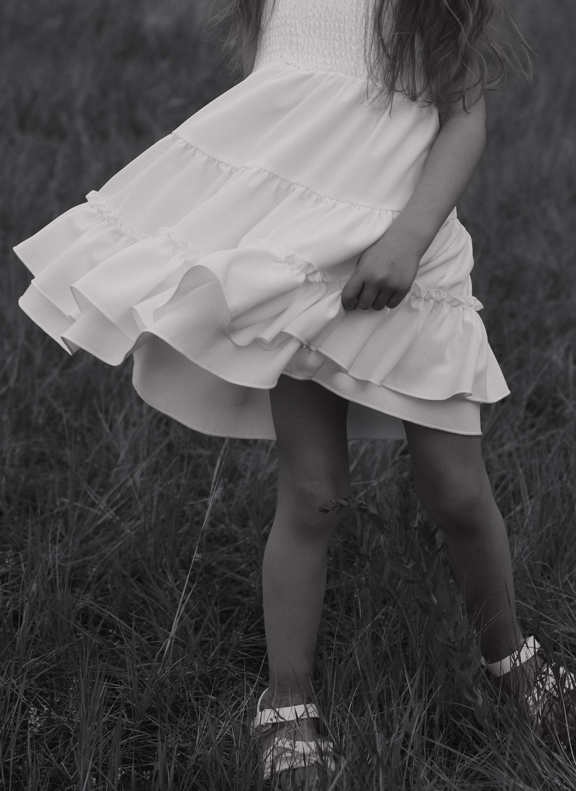 Young girl in white ruffled dress twirling in a field, black and white photo.