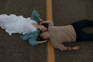 An aerial view of a couple lying on pavement beside a yellow road line, sharing a tender moment in a couples photo session.