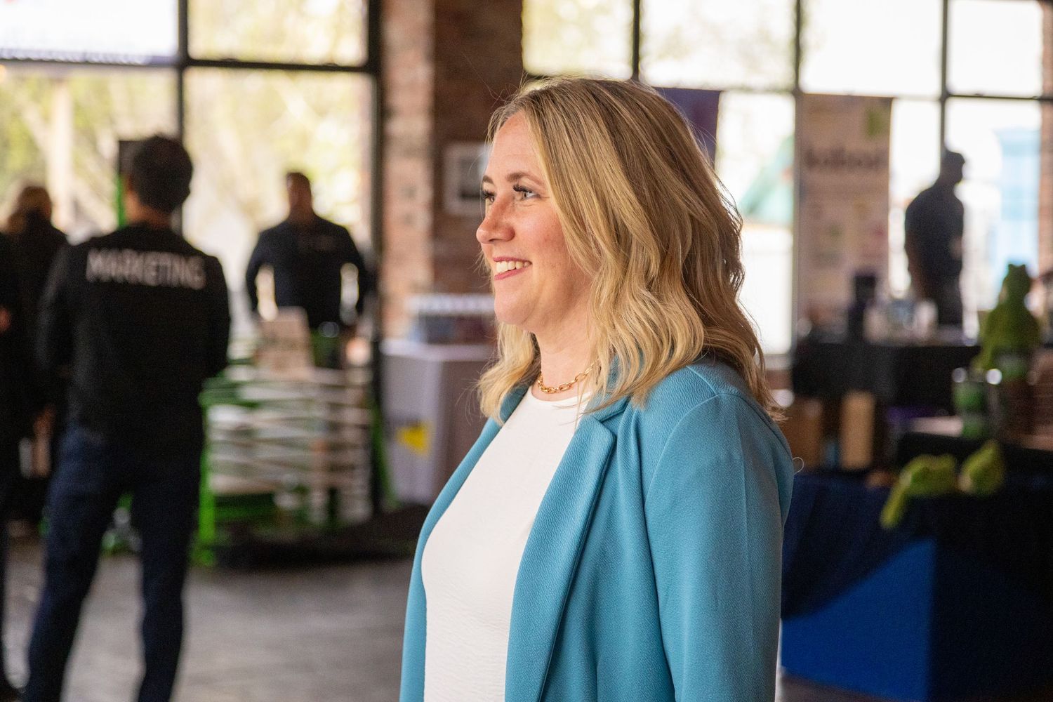 Professional woman in teal blazer smiling at a marketing business event in a modern industrial space.