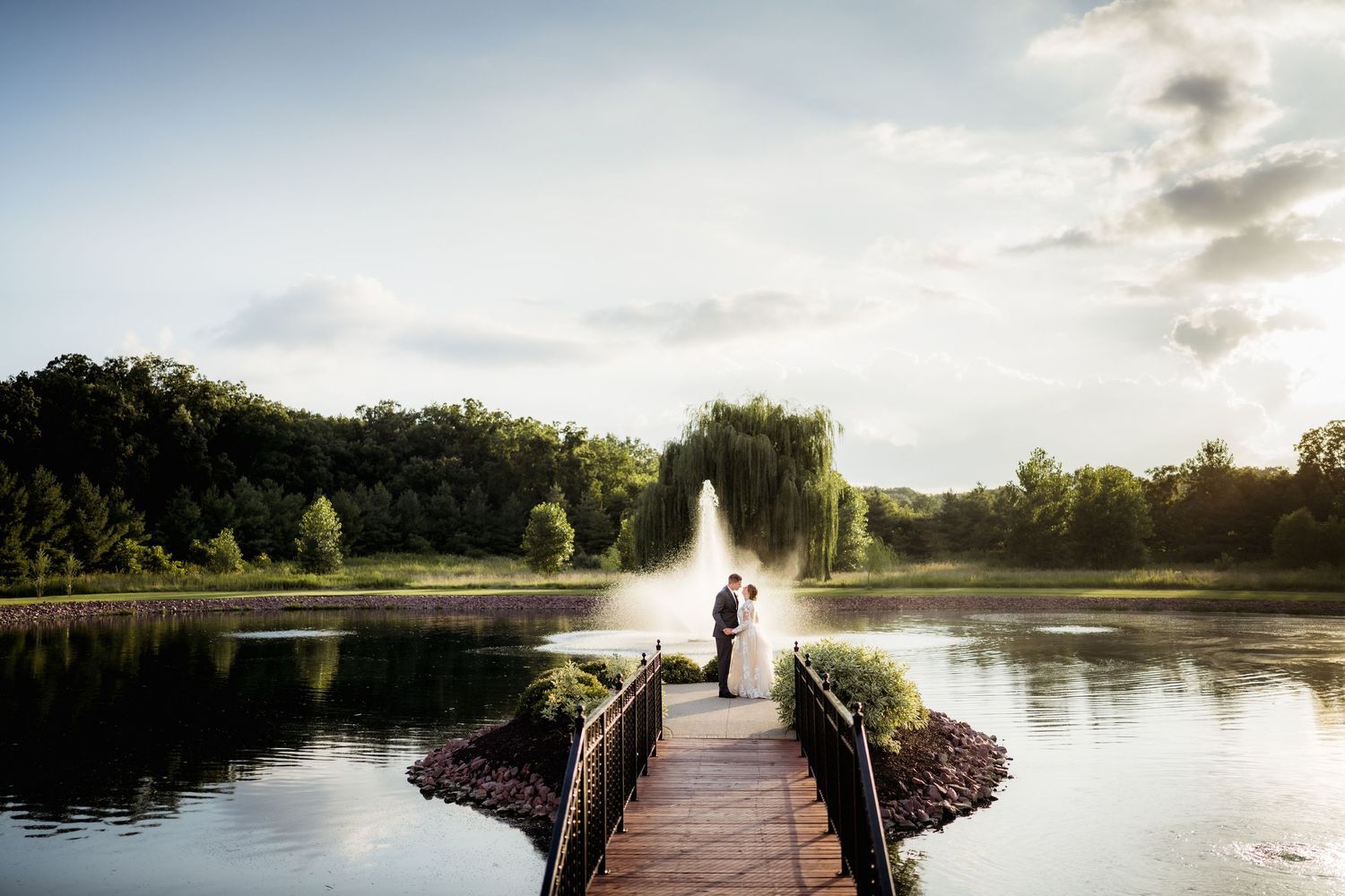 A red barn wedding venue surrounded by lush green lawns and a pond on a sunny day.