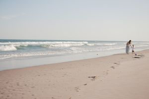 Mother and child walking along a serene sandy beach with ocean waves.
