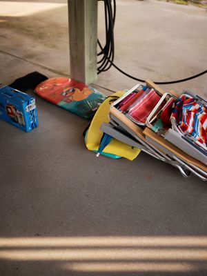 Beach gear including folding chairs, umbrella, and toys piled on garage floor before outing.